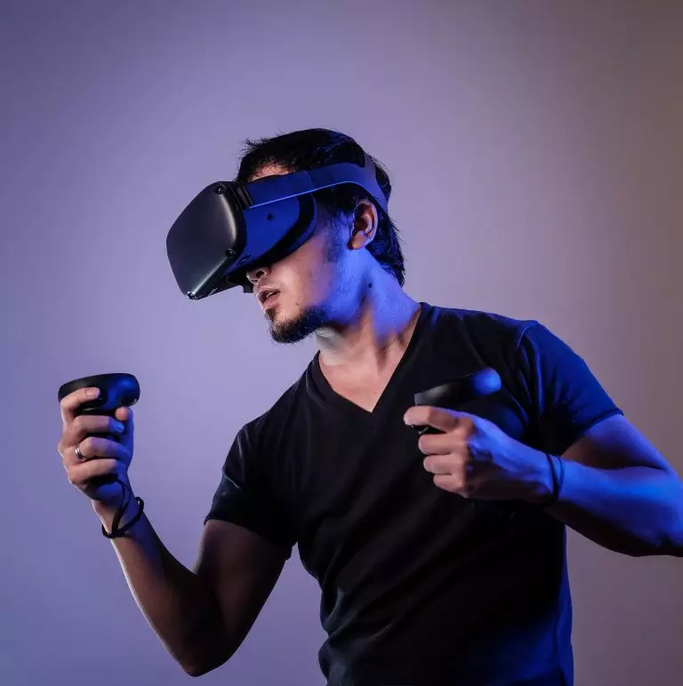 A man in a black crew neck t shirt uses haptic controllers and wears a VR headset