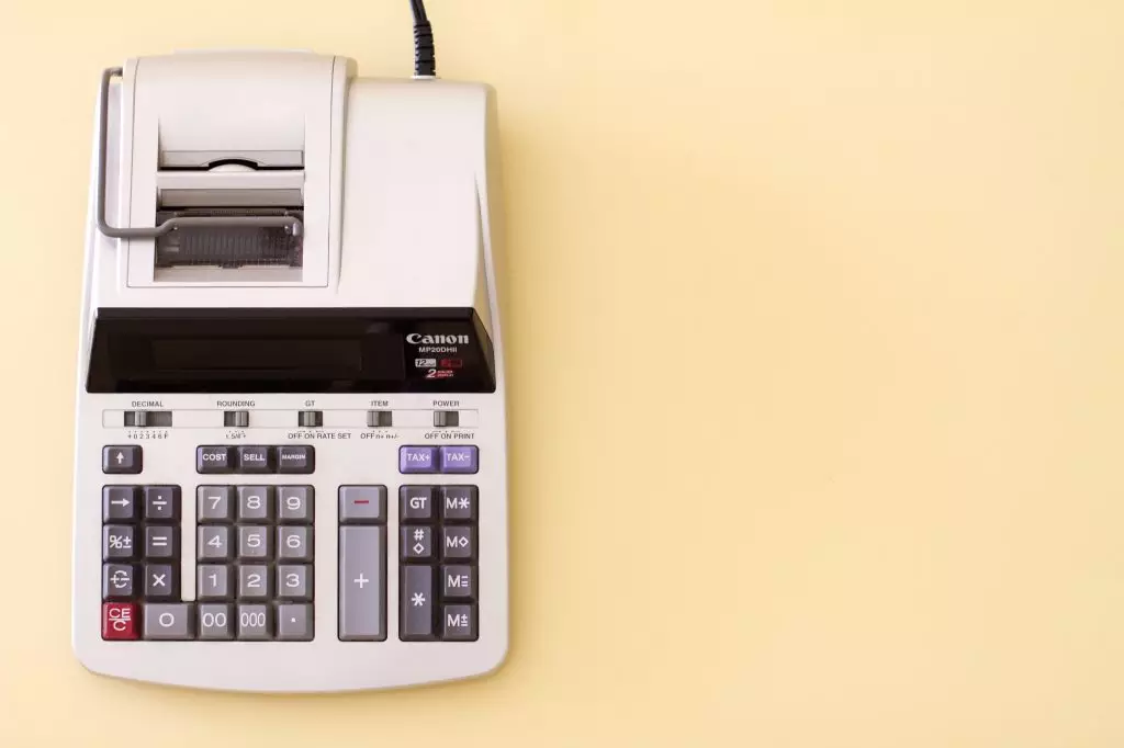 A white cannon accounting calculator sits on a creamy yellow desk.
